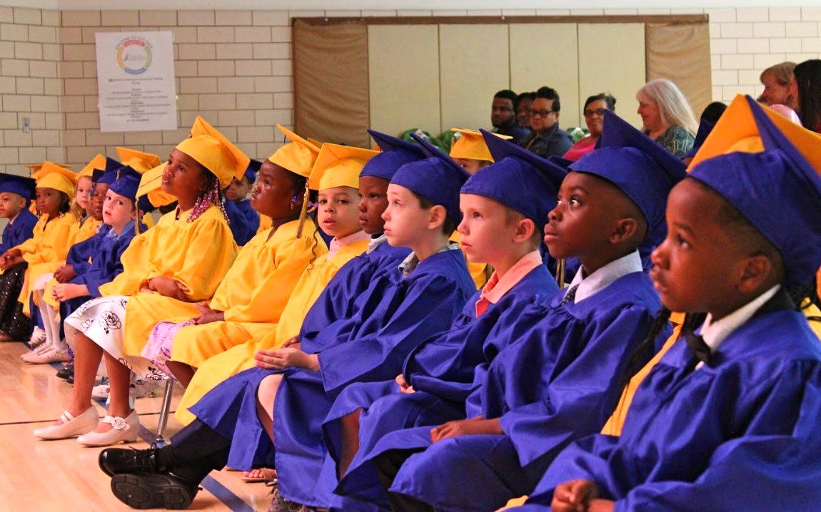 Estudiantes de kindergarten de PHCSE con togas y birretes en su ceremonia de graduación