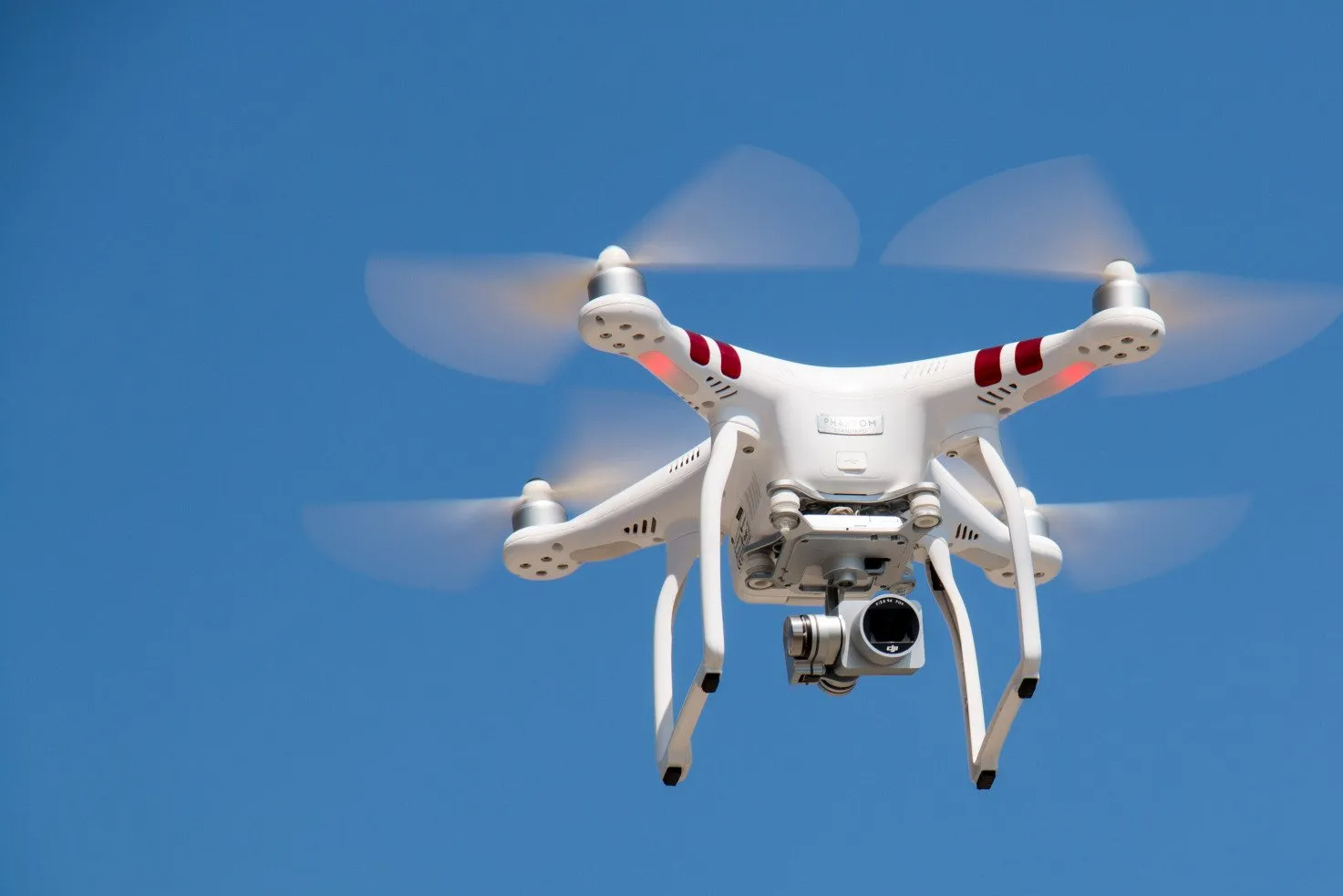 A white quadcopter drone flying against a clear blue sky